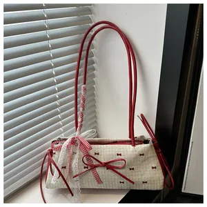 Détail du sac beige avec nœuds rouges, dentelle blanche et ruban à carreaux décoratif