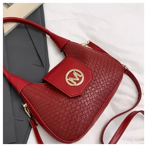 Detail of burgundy textured leather bag with circular gold M logo and curved flap