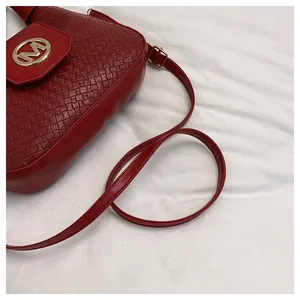 Detail of red crossbody bag featuring woven texture and a gold metal M buckle