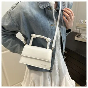 Weiße quadratische Umhängetasche aus Leder mit Knotengriff am Model in Jeansjacke