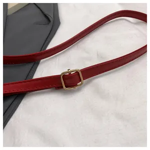 Detail of red faux leather shoulder strap with gold buckle and fine stitching