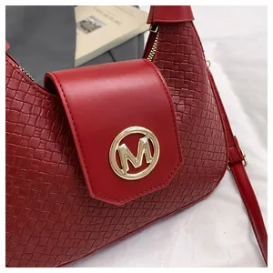 Detail of burgundy stone texture shoulder bag with gold M buckle and braided finish