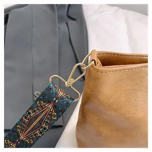 Detail of wide ethnic pattern strap and gold hardware on a tan textured tote bag