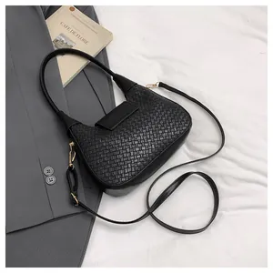 Detail of black woven shoulder bag with adjustable straps on a minimalist background