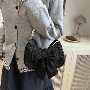 Elegante borsa a mezzaluna nera con fiocco e manico in perle bianche su sfondo bianco