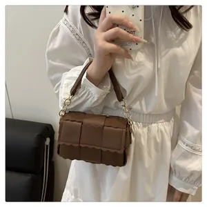 Brown woven crossbody bag with wavy edge detailing and gold chain link strap on white dress