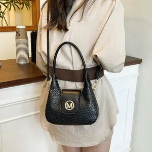 Chic black stone texture handbag with golden M buckle worn as a crossbody shoulder bag
