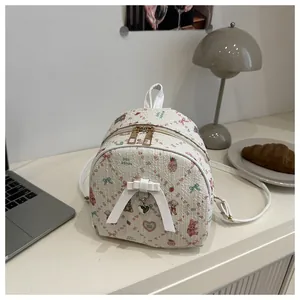 Detailed view of mini cream backpack with pink strawberry prints and bow charm on a desk