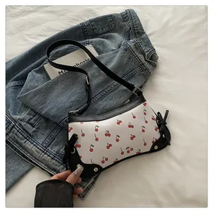 Dettaglio della borsa a sella con stampa a ciliegie e fiocchi neri su giacca denim