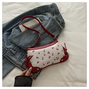 Dettaglio della borsa a sella con stampa a ciliegia, fiocco laterale rosso e texture in PU