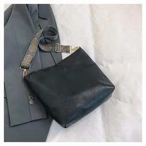 Detail of a black leather bucket bag featuring a colorful vintage pattern wide strap