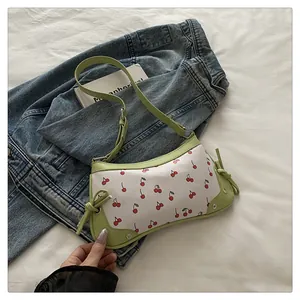 Dettaglio delle stampe di ciliegie rosse sulla borsa a tracolla verde chiaro su denim