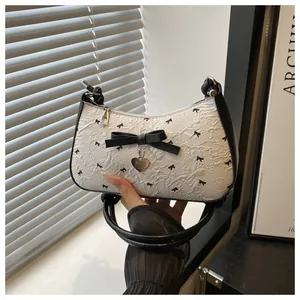 Détail du tissu plissé blanc avec motifs de nœuds noirs et breloque coeur en métal