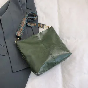 Detail of dark green tote bag with ethnic pattern wide strap on grey blazer background