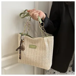 Dettaglio della borsa tote in paglia intrecciata con finiture in pelle verde e catena d'oro