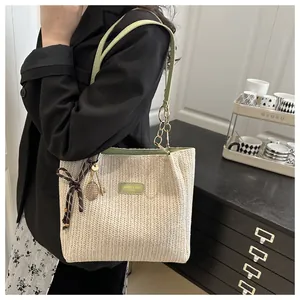 Dettaglio della borsa tote in paglia con etichetta in pelle verde, catena e foulard