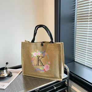 Detailansicht der beigen Jute-Einkaufstasche mit Blumenkranz und K-Buchstabendruck-Motiv