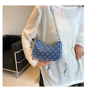 Close-up of denim shoulder bag with white bow print and silver metal chain strap