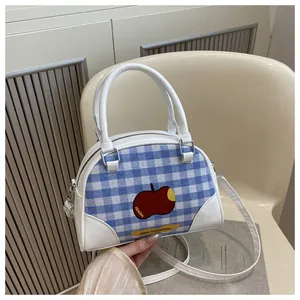 Close-up of blue plaid crossbody bag with red apple print on a white seat