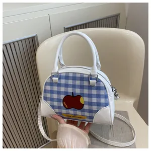 Detail of white leather and plaid handbag with red apple print on a minimalist chair