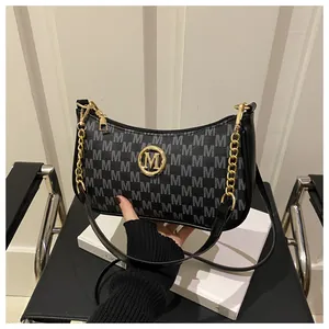 Detail of black underarm bag with grey M patterns and gold logo on a modern chair