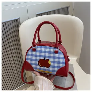 Detail of red leather and blue plaid canvas crossbody bag with apple print on chair