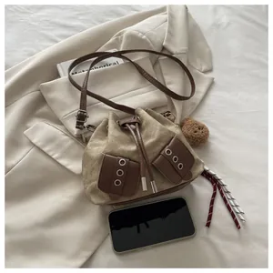 Detail of drawstring canvas bucket bag with leather pockets and decorative plush ball charm
