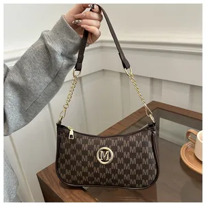 Detail of dark brown leather underarm bag with M pattern and golden metal logo
