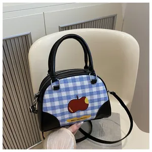 Detail of blue and white checkered crossbody bag with red apple print and black leather strap