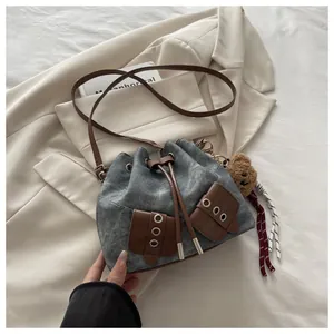 Close-up of vintage blue denim bucket bag with brown leather details and plush bear charm