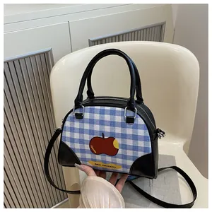 Detail of checkered crossbody bag featuring a red apple patch and black leather trim