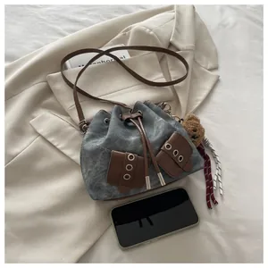 Detail of grey denim bucket bag with brown leather pockets and plush bear charm