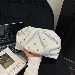 White pleated cloud clutch bag with gold studs in a minimalist lifestyle setting