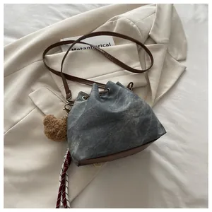 Detail of drawstring bucket bag with washed denim fabric and brown leather trim