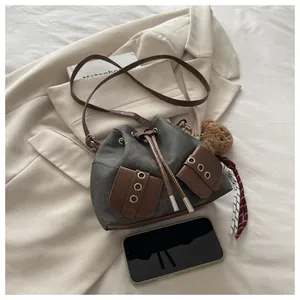 Detail view of canvas bucket bag with drawstring closure and plush bear accessory