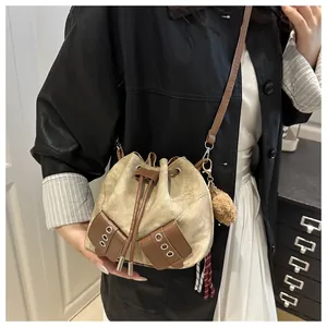 Detail of beige canvas bucket bag with brown leather trim and plush charm accessory