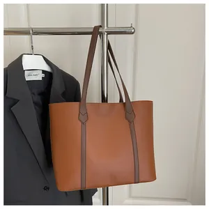 Close-up of brown faux leather tote bag with dark handles and a grey blazer background