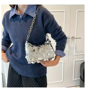 Close-up of a silver sequin shoulder bag with thick gold chain worn by a model