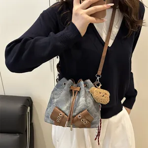 Chic drawstring bucket bag in blue denim and brown leather with cute bear charm