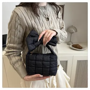 Detail of a black quilted puffer handbag featuring a large decorative bow and metal zipper