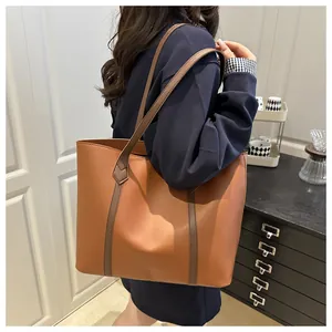 Detail of a large brown color-block PU leather tote bag worn by a model in a modern room
