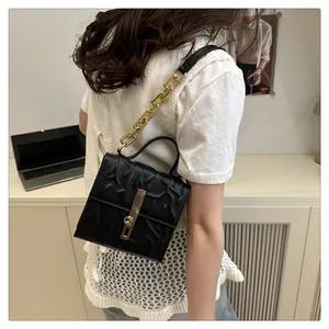 Detail of black textured handbag featuring gold chain strap and metallic buckle closure