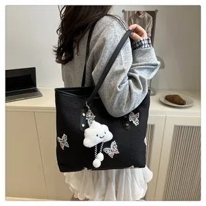 Detail of black tote bag with butterfly embroidery and cute cloud plush pendant accessory