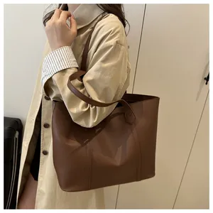 Brown leather tote bag worn on shoulder by a model in a minimalist indoor setting