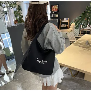 Side view of a black canvas tote bag with white lettering worn over the shoulder