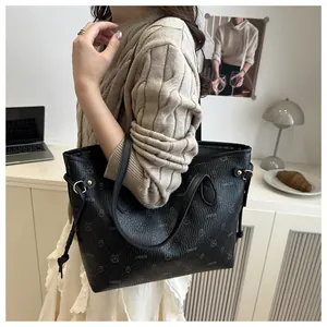 Vue détaillée du sac cabas noir avec texture litchi, lettrage de marque et cordons latéraux