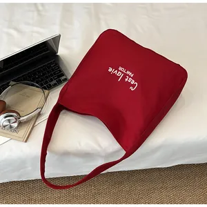 Flat lay of red canvas tote bag with C'est la vie text next to a laptop and headphones