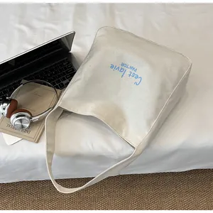 Detail of off-white canvas tote bag featuring artistic blue C'est la vie printed text