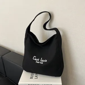 Minimalist black canvas tote bag with C'est la vie print shown in a studio setting