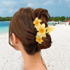 Tropical plumeria flower hair claw clip securing a bun hairstyle against a beach background